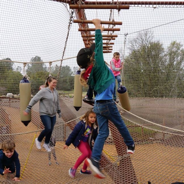 Children enjoying an outdoor adventure park obstacle course with ropes and nets.