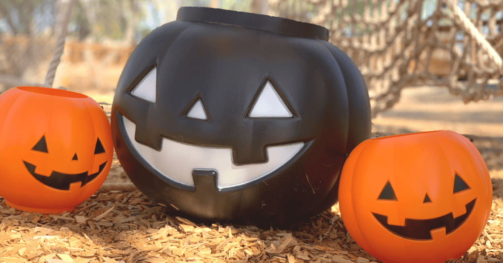 Three Halloween pumpkin decorations, two orange and one large black, displayed on a bed of wood chips at a quarry with a blurred natural background.