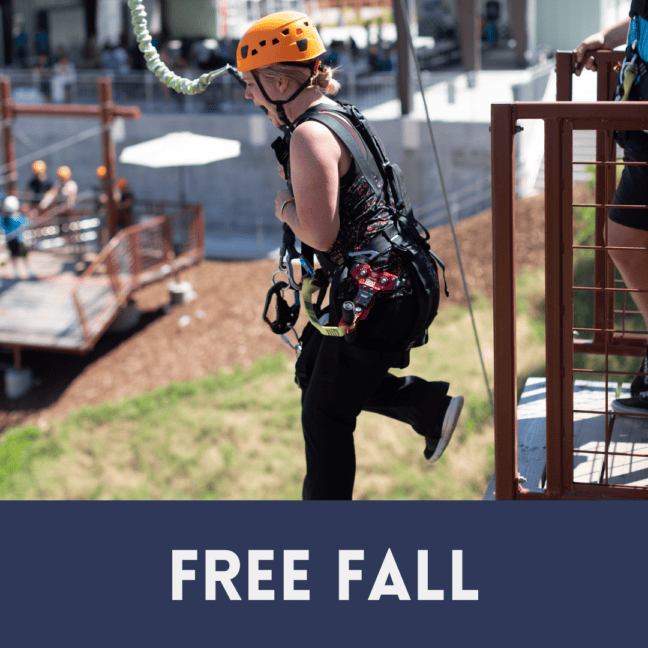 A park guide in a helmet and harness jumps off a platform during a free fall activity, with "free fall" text overlay.