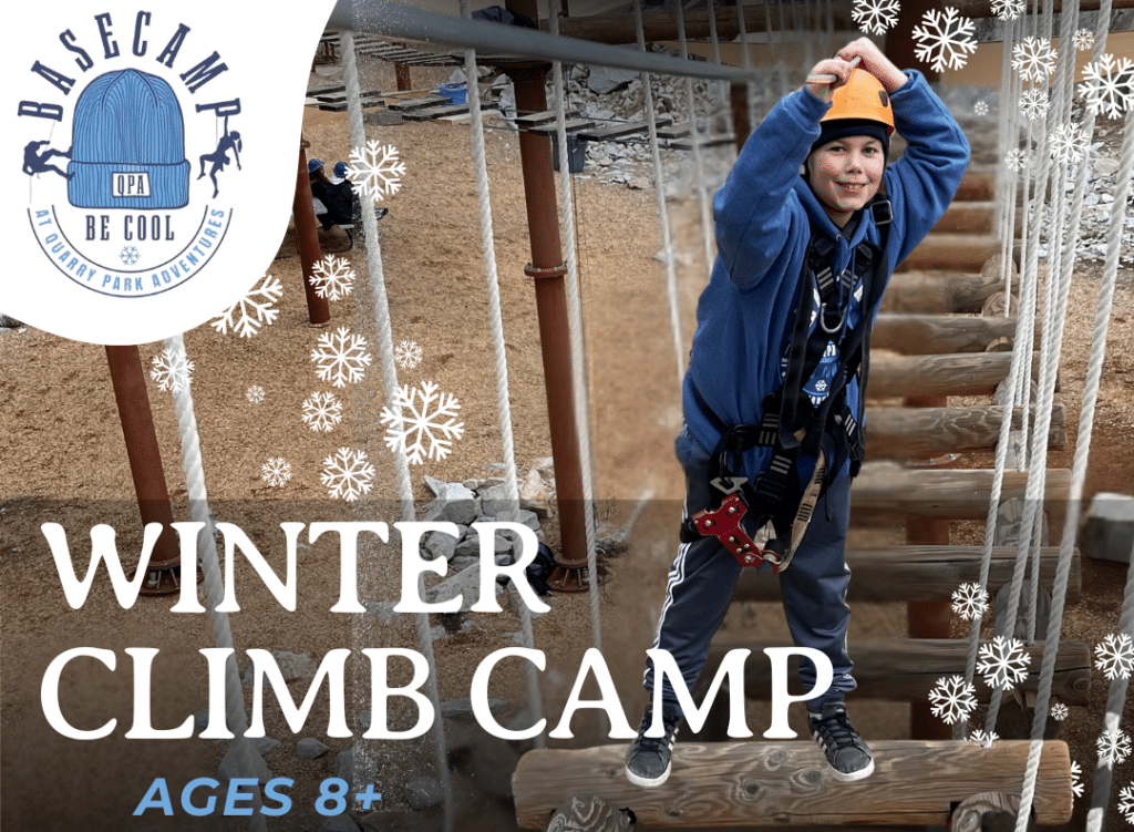 A child, securely strapped in a safety harness and helmet, navigates the rope course at the Winter Climb Camp. Surrounded by snowflake decorations, the sign proudly welcomes adventurous campers ages 8 and up, offering an unforgettable winter experience.