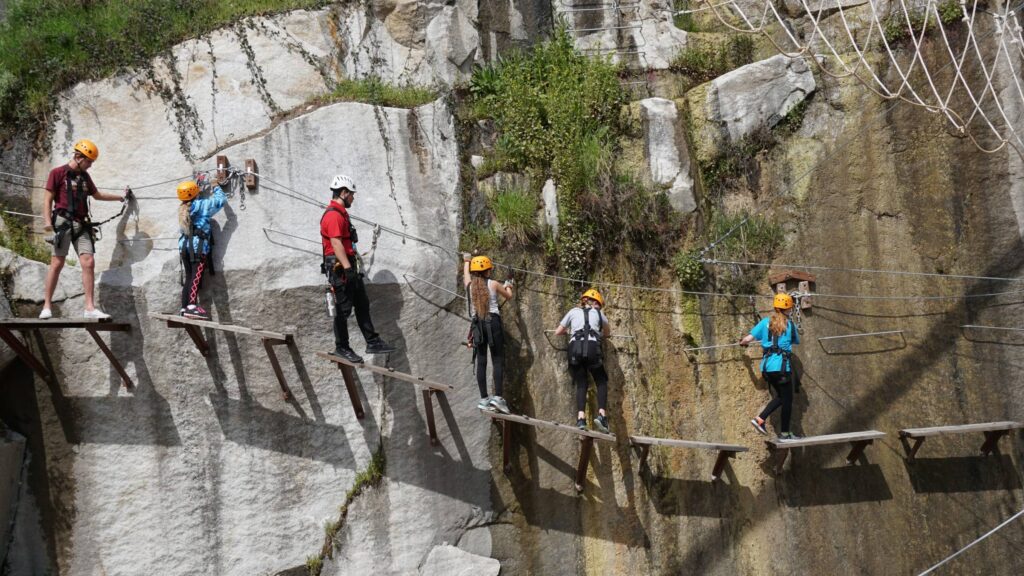 Adventurers wearing helmets navigate a cliffside ropes course as part of our New Year special, crossing wooden planks with safety harnesses while enjoying big savings.