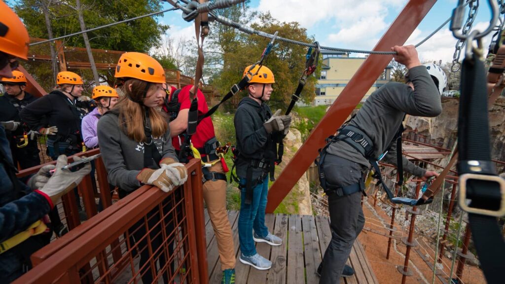 People wearing safety gear and helmets are preparing to zip line from a wooden platform, eager to start the New Year with thrilling adventures.