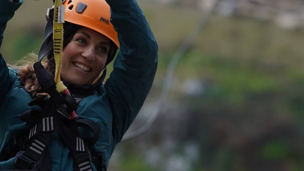 A person wearing a helmet and safety gear smiles, savoring the exhilarating rush of zip-lining outdoors. It's the perfect way to embrace the New Year with adventure while enjoying savings on thrilling experiences.