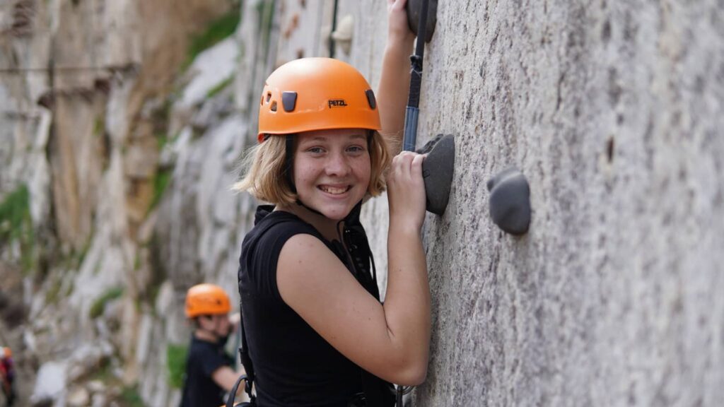 Climbing a rock wall with a grin, wearing a bright orange helmet, this adventurer captures the spirit of new beginnings—like enjoying big savings in the New Year.