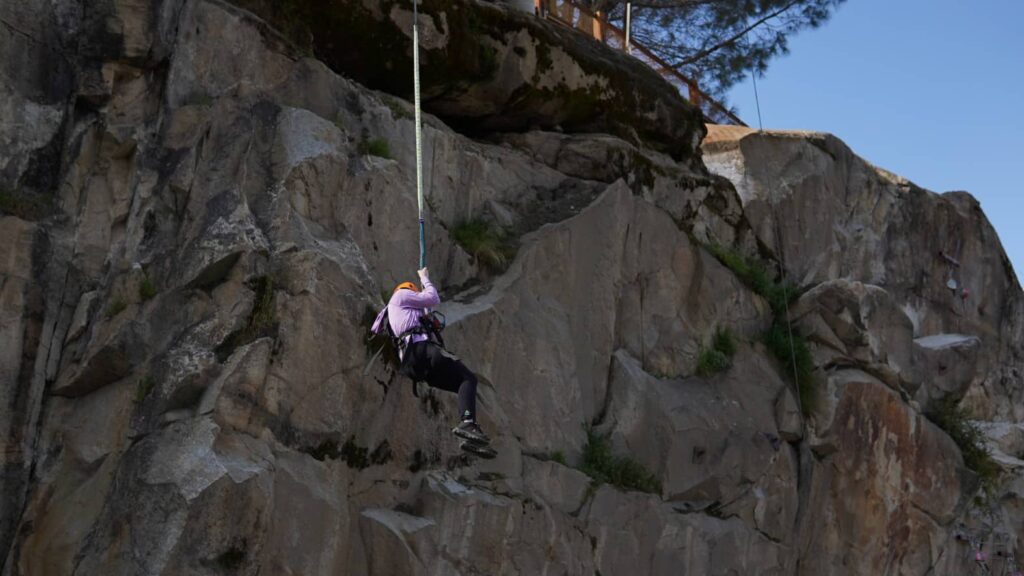 Under a clear blue sky, a person in helmet and harness rappels down a rocky cliff, embracing the thrill of new challenges and fresh starts, much like the excitement of New Year adventures.