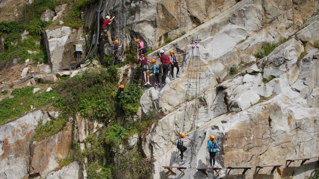 A group of people wearing helmets and harnesses climb a steep rock face on a via ferrata route, conquering new heights like resolutions in the New Year.